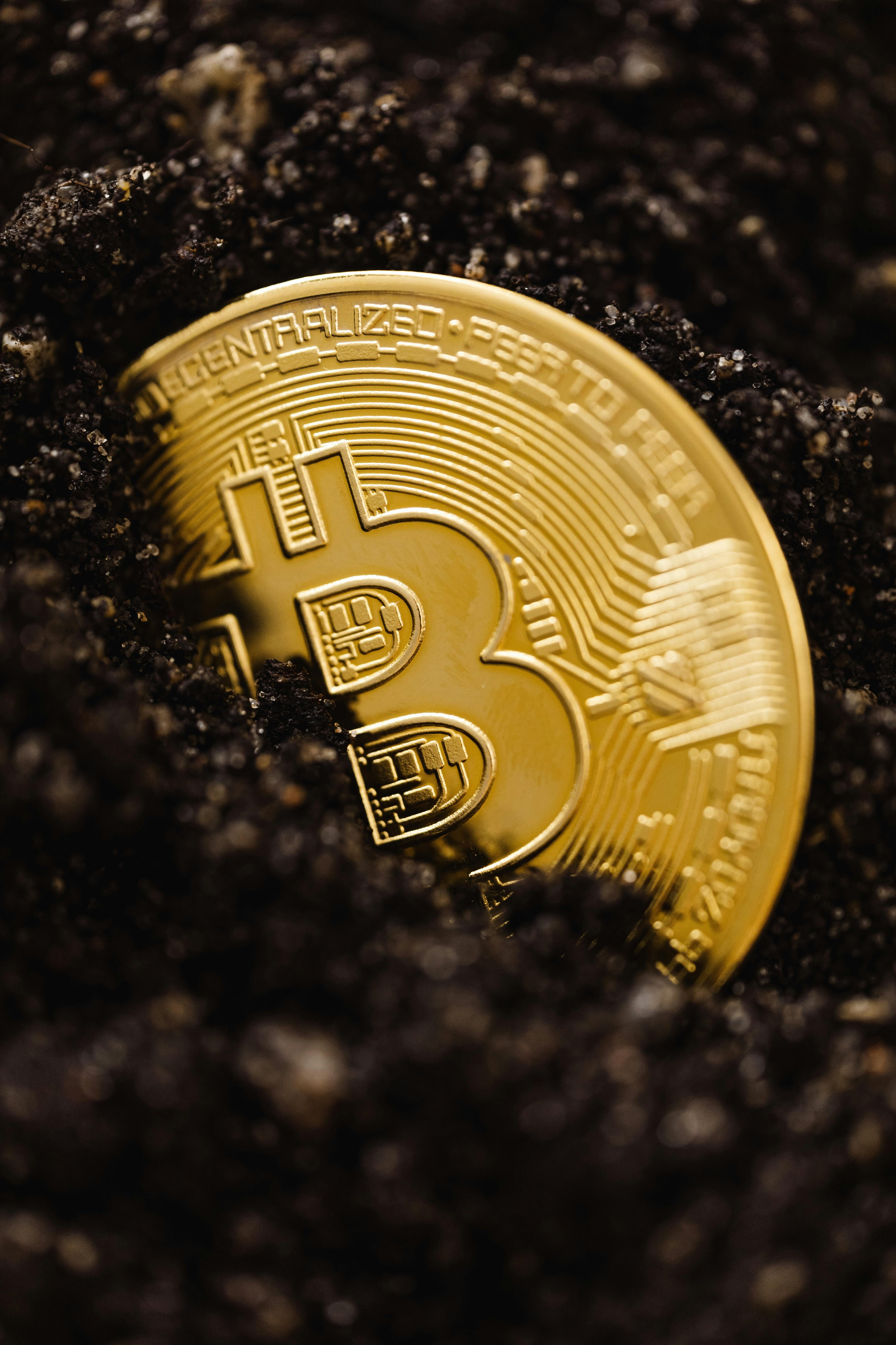 Moneda dorada de Bitcoin medio enterrada en tierra oscura, símbolo de valor oculto e inversión cripto a largo plazo.